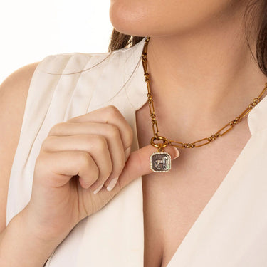 Necklace with a square pendant worn by a person in a white outfit.