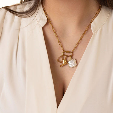 Gold necklace with charms worn by a person in a light-colored outfit