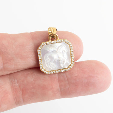 Gold pendant with a white stone held between fingers on a white background
