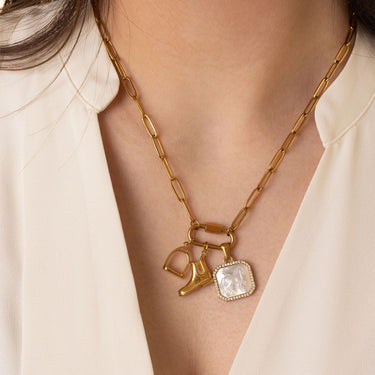 Gold necklace with shoe and square pendant on a person wearing a beige top.