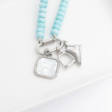 Silver blue beaded necklace with horse, stirrup and boot charms on a white background