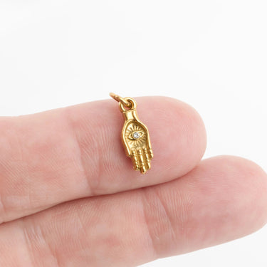 Gold hand-shaped pendant with a diamond on a finger against a white background
