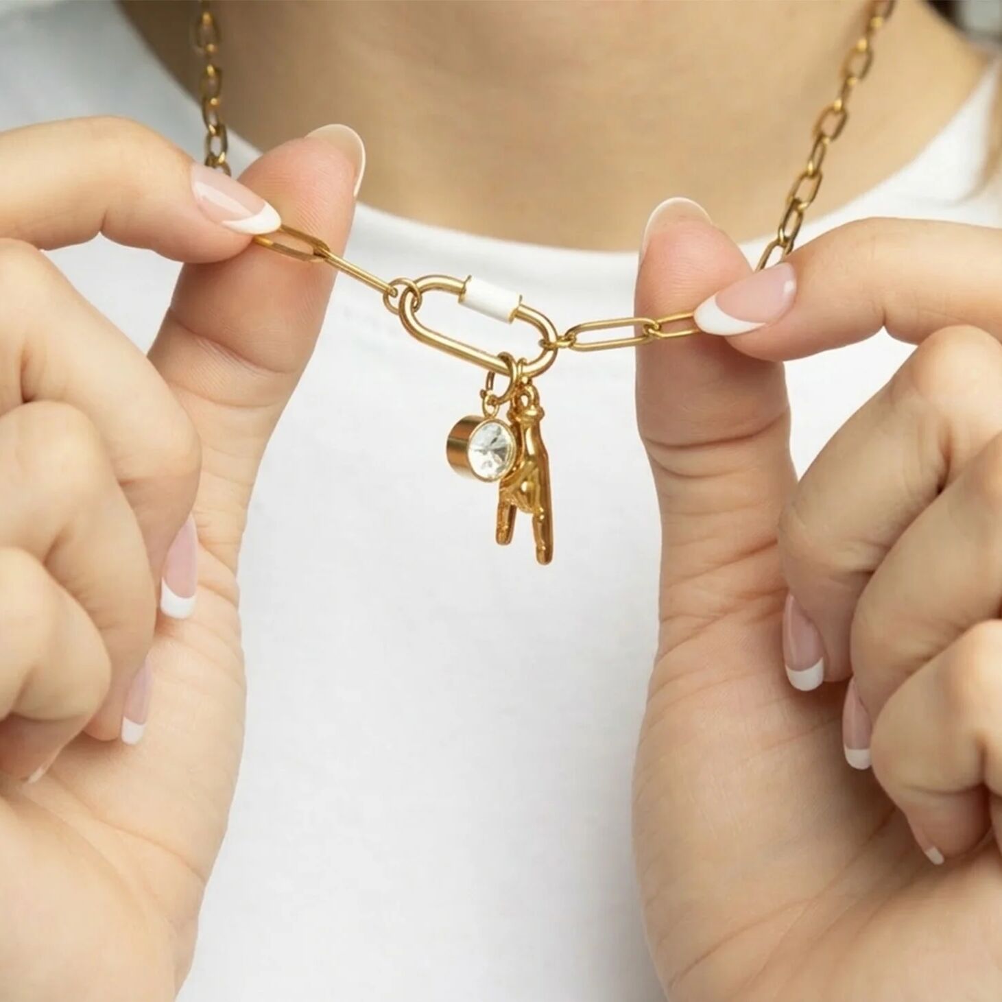 Gold chain necklace with key and heart charm held by hands against a white background