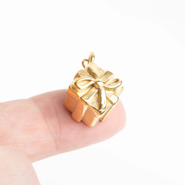 Gold gift box pendant on a finger against a white background