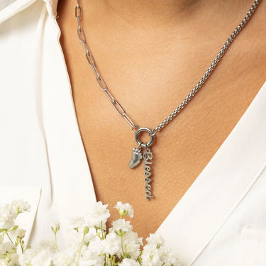 Silver necklace with Baby Foot Charm and 'blessed' charm worn by a person, with white flowers in the foreground.