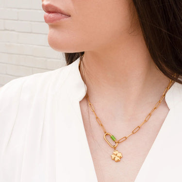 Gold chain necklace with a clover pendant worn by a person against a neutral background