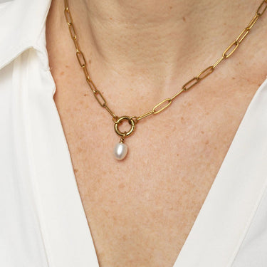 Gold chain necklace with a pearl pendant on a person wearing a white shirt.