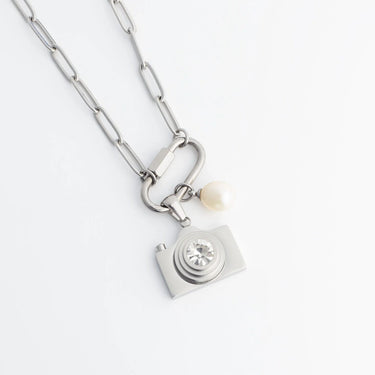 Silver necklace with a camera charm and pearl on a white background