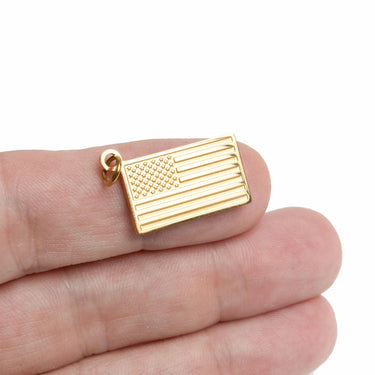 Gold American flag pendant held between fingers on a white background