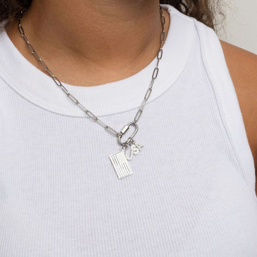 Silver chain necklace with Flag Charm and pave U.S.A letter charms worn by a person in a white tank top.