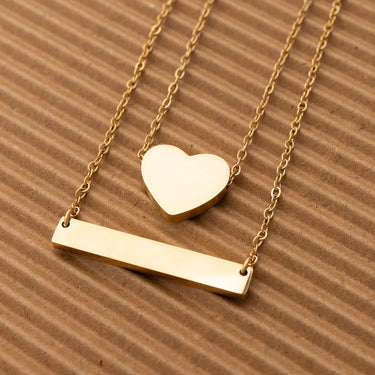 Gold necklace with heart and bar pendants on a brown textured background