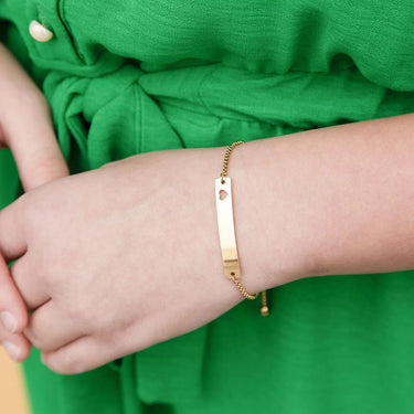 Gold bracelet on a wrist with a green garment in the background