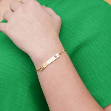 Gold bracelet with a heart cutout on a green fabric background