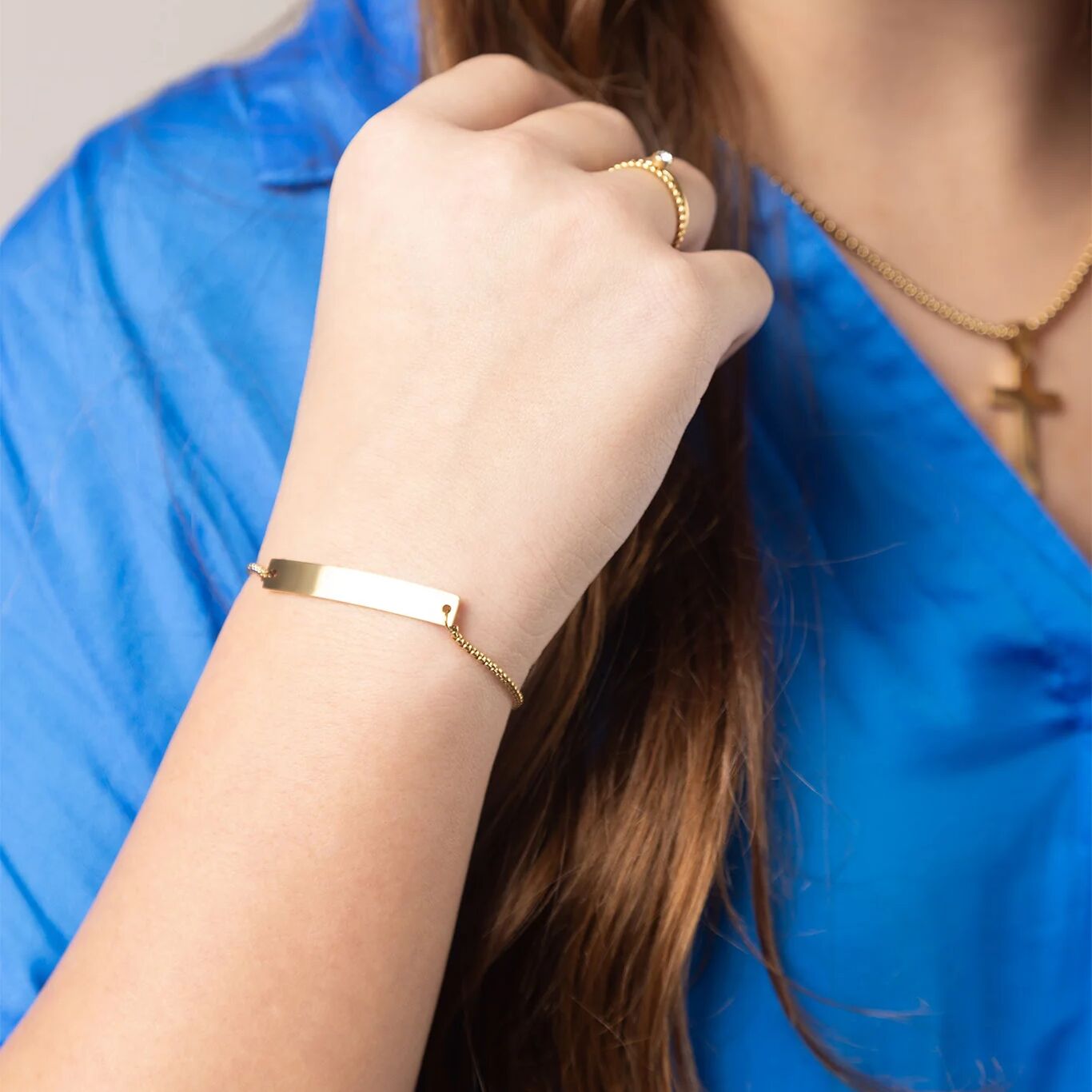 Person wearing a gold bracelet and ring, holding hair with a blue background