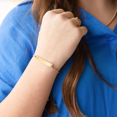 Close-up of a person wearing gold jewelry including a bracelet and ring, with a blue garment.