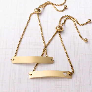 Gold necklace with heart and bar pendants on a light wooden surface