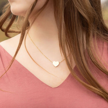 Close-up of a person wearing a gold necklace with a heart pendant, outdoors.
