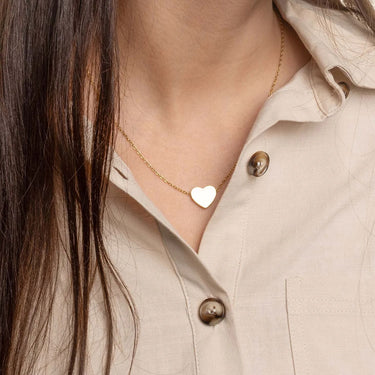 Necklace with a heart-shaped pendant worn by a person in a beige shirt.