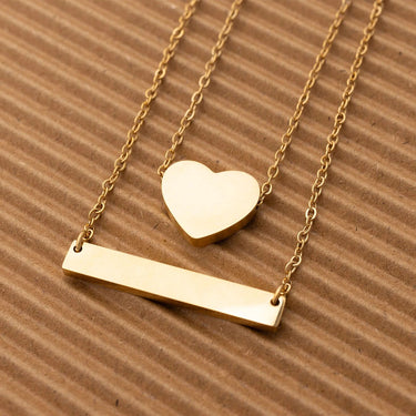 Gold necklace with heart and bar pendants on a brown textured background