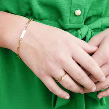 Close-up of hands with gold bracelet and ring against a green background