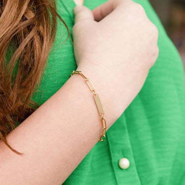 Gold bracelet on a wrist with a green background
