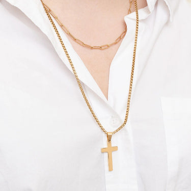 Gold cross necklace worn by a person on a white shirt background