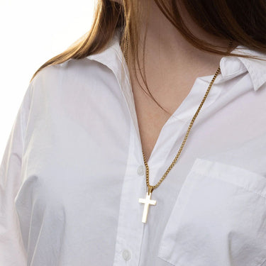 Gold necklace with a cross pendant worn by a person in a white shirt.