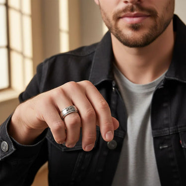 Man wearing a black jacket and gray shirt with a close-up of his hand showing two rings.