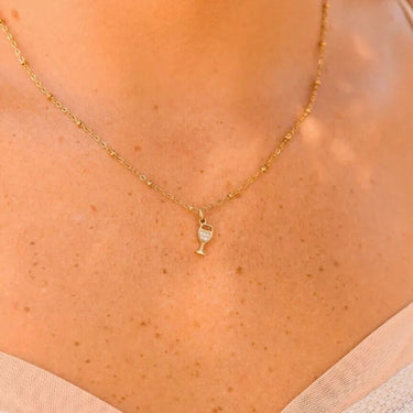 Gold necklace with a wine glass pendant on a person's neck
