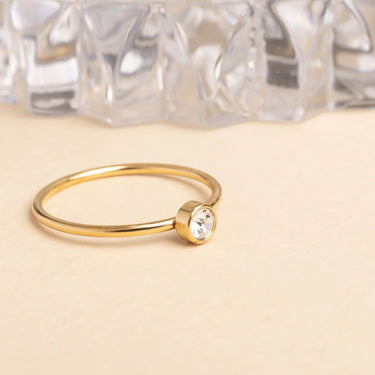 Gold ring with a small gemstone on a beige surface with crystal background