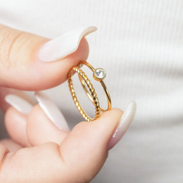 Gold ring with a diamond held between fingers against a neutral background