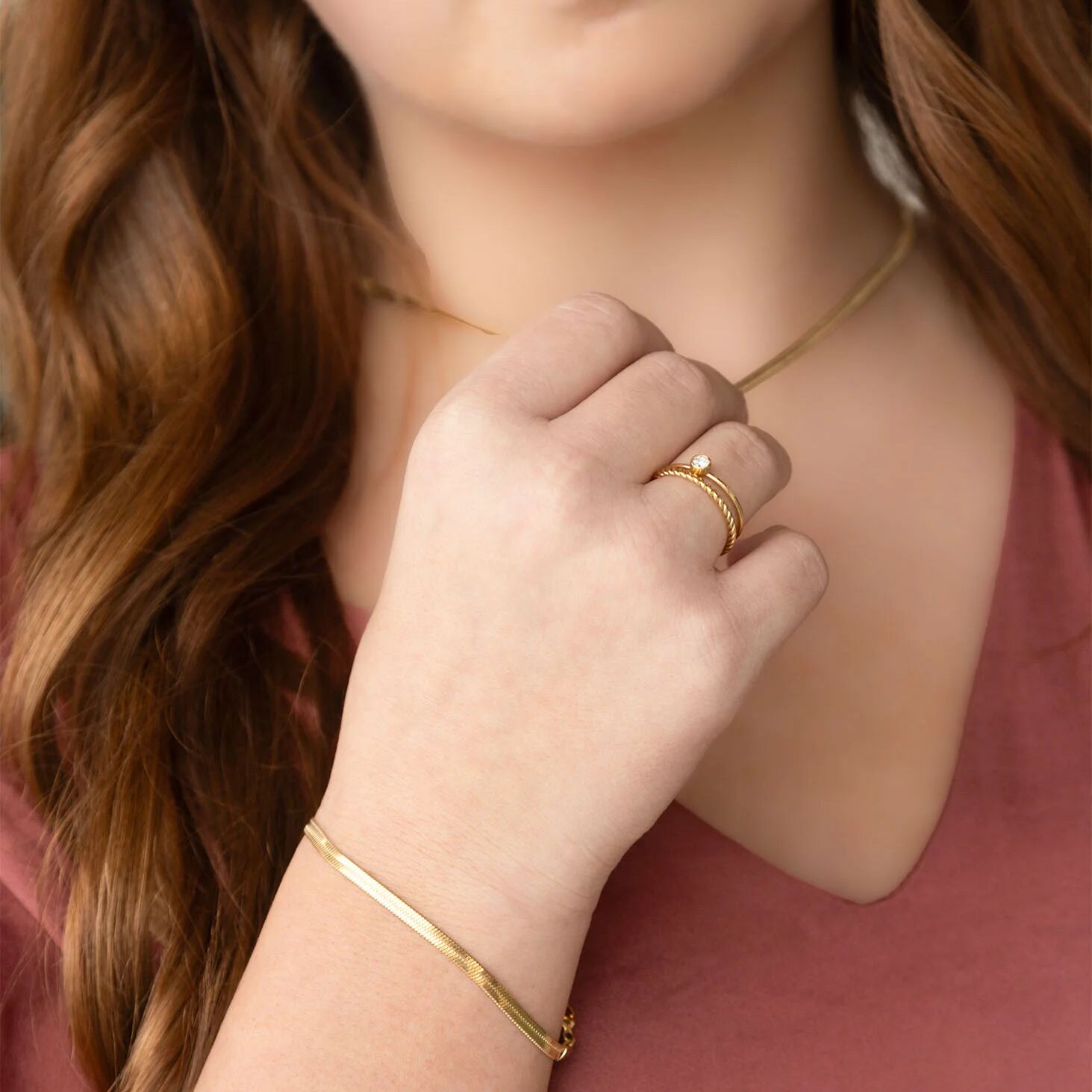 Close-up of a person wearing gold jewelry including a necklace, ring, and bracelet.
