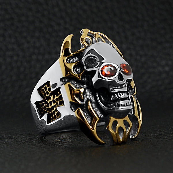 Stainless steel red Cubic Zirconia eyed flaming skull with 18K gold PVD Coated accents and Maltese Cross ring angled on a black leather background