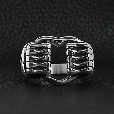 Stainless steel polished heart gripped by bone hands ring on a black leather background.