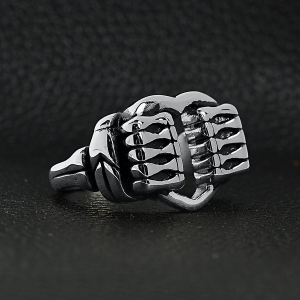 Stainless steel polished heart gripped by bone hands ring angled on a black leather background.