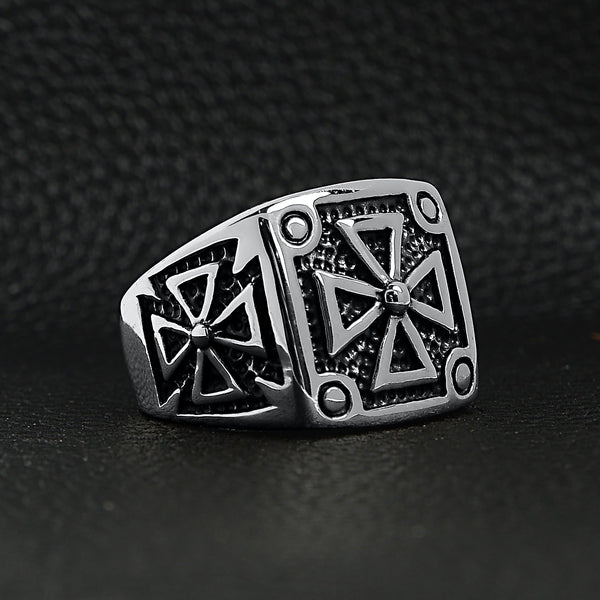 Stainless steel polished Maltese Cross ring angled on a black leather background.