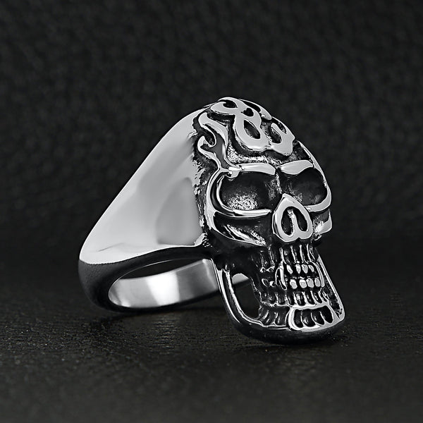 Stainless steel polished flaming skull ring angled on a black leather background.