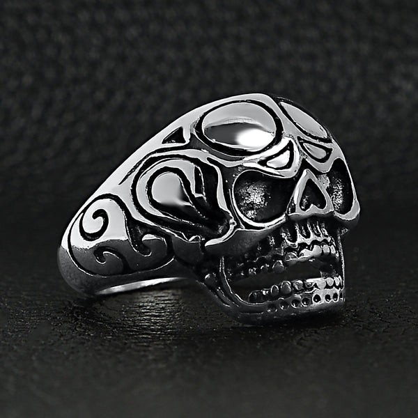 Stainless steel polished filigree skull ring angled on a black leather background.
