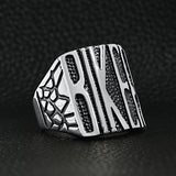 Stainless steel polished "BIKER" men's ring angled on a black leather background.
