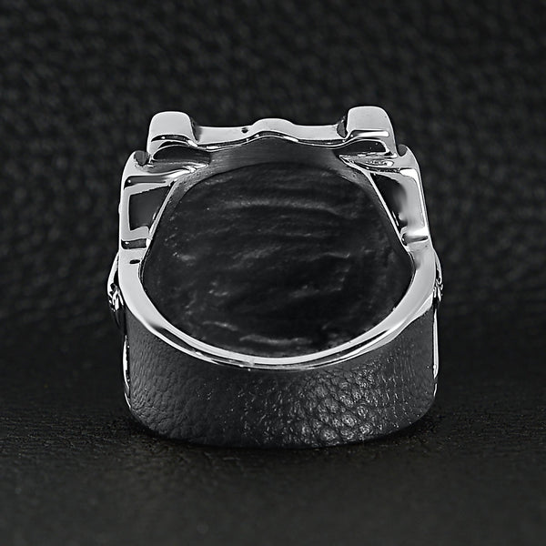Stainless steel polished studded skull ring back view on a black leather background.
