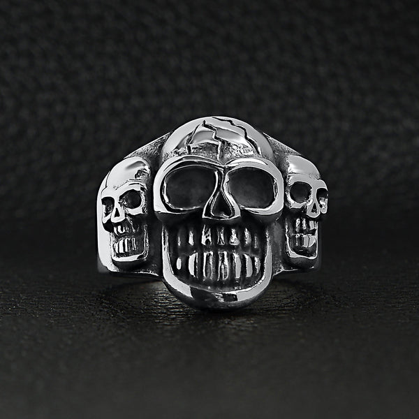 Stainless steel polished cracked triple skulls ring on a black leather background.