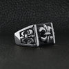Stainless steel polished black Fleur De Lis ring angled on a black leather background.