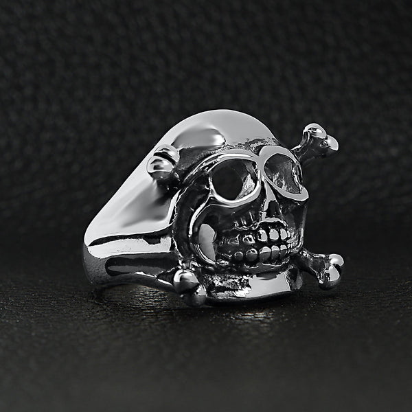Stainless steel skull and crossbones ring angled on a black leather background.