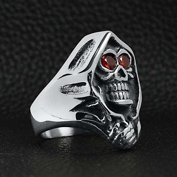 Stainless steel red Cubic Zirconia eyed grim reaper ring angled on a black leather background.