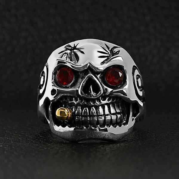 Stainless steel 18K gold plated bullet cigar smoking red Cubic Zirconia eyed skull ring on a black leather background.