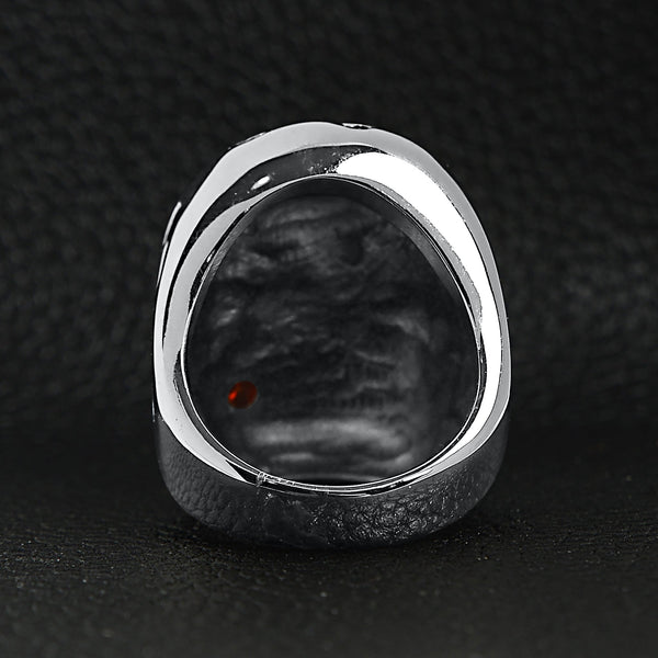 Stainless steel large filigree skull biting red Cubic Zirconia rose ring back view on a black leather background.