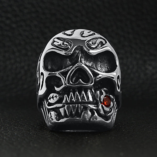 Stainless steel large filigree skull biting red Cubic Zirconia rose ring on a black leather background.