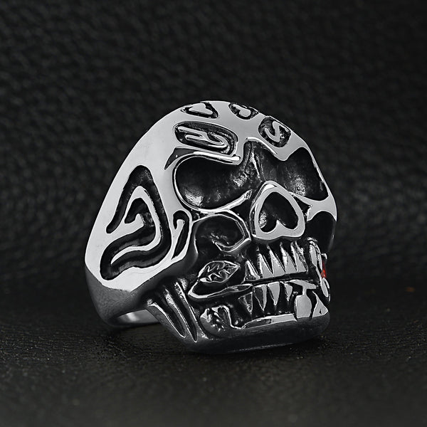 Stainless steel large filigree skull biting red Cubic Zirconia rose ring angled on a black leather background.