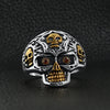 Stainless steel 18K gold PVD Coated red Cubic Zirconia eyed filigree skull ring on a black leather background.