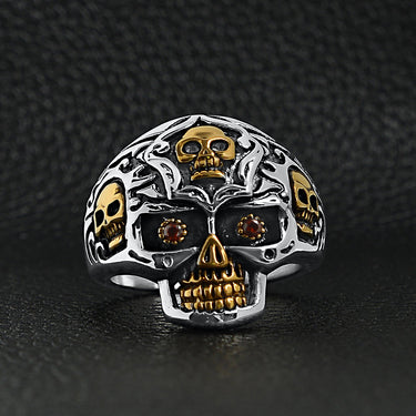 Stainless steel 18K gold PVD Coated red Cubic Zirconia eyed filigree skull ring on a black leather background.